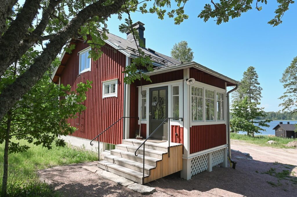 Ett rött hus med trädfärgade trappor med skärgården i bakgrunden.